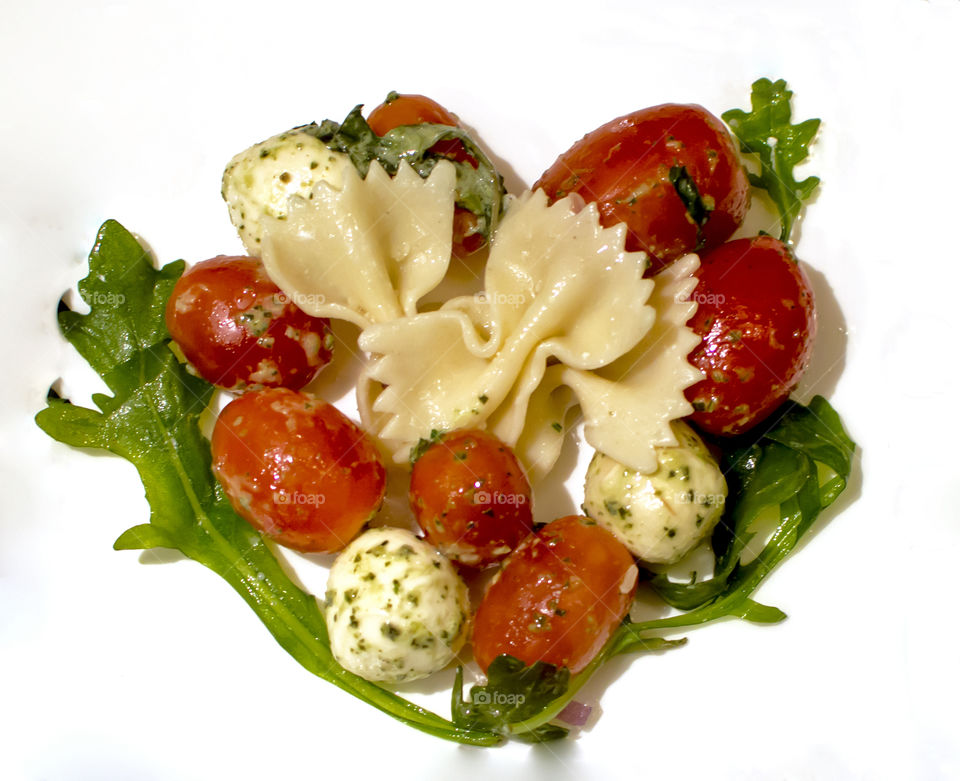 Pasta salad with fresh herbs and olive oil, garden fresh tomatoes and cheese  in heart shape ready to eat on plate 