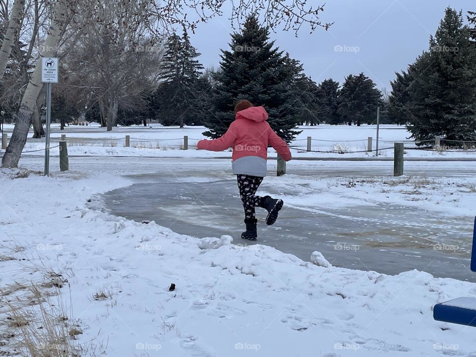 This young 8 yr old girl, is having fun, running, sliding, and skating in her black winter boots and peach color jacket, on this icy walkway, going to a park, in Medicine Hat, Alberta, Canada, on this nice winter day