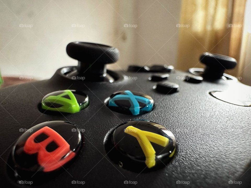 Black Xbox controller focusing its colored buttons while the natural light enters through the window.