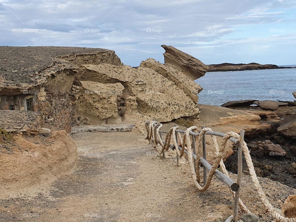 a fence at the coast made of thick ropes leads to a habitation in the rock