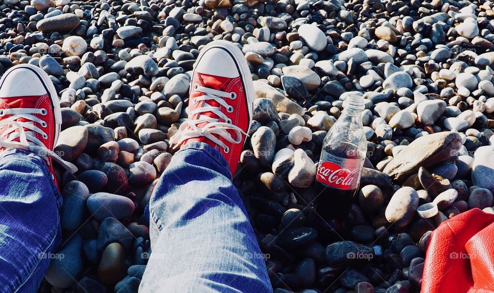 A bottle of Diet Coke on the beach with red sneakers.