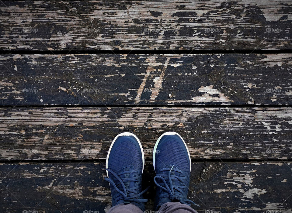 Top view of human feet with sneakers standing on old wood floor background with copy space.