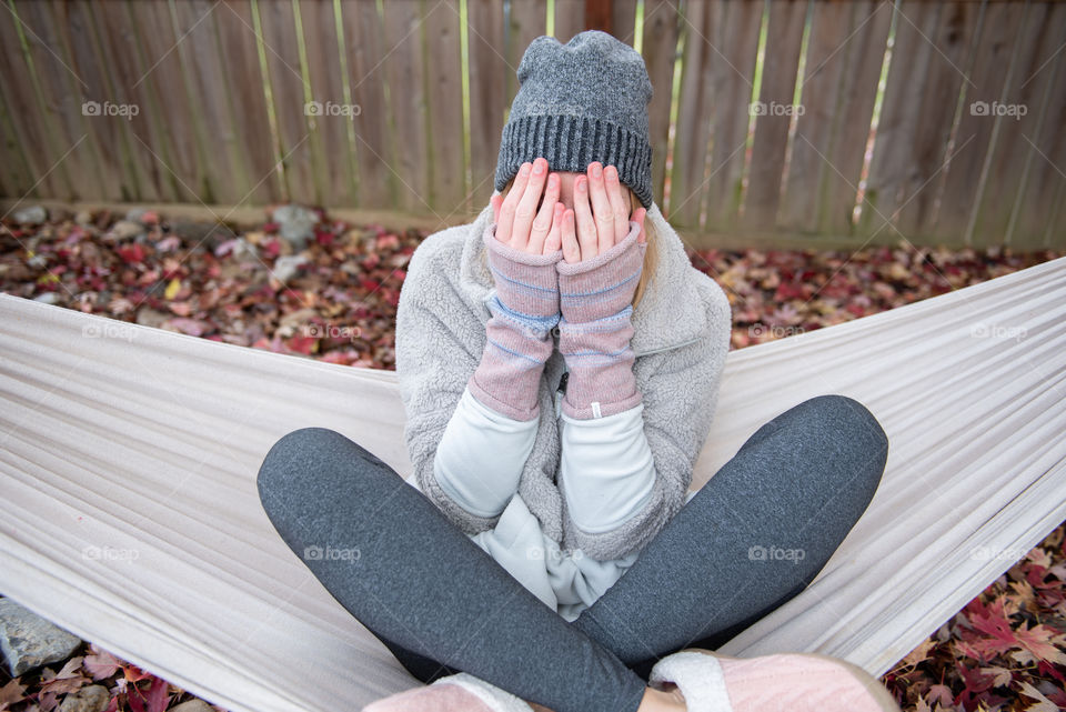 Young millennial woman sitting in a hammock in the fall and covering her face with fingerless gloves