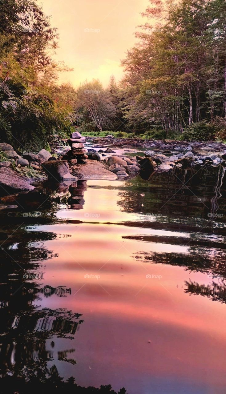 inuksuk on the rocks by the river at sunset.