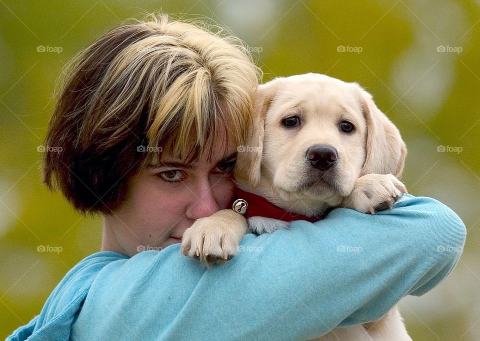 A young girl holds her yellow lab puppy at a park.