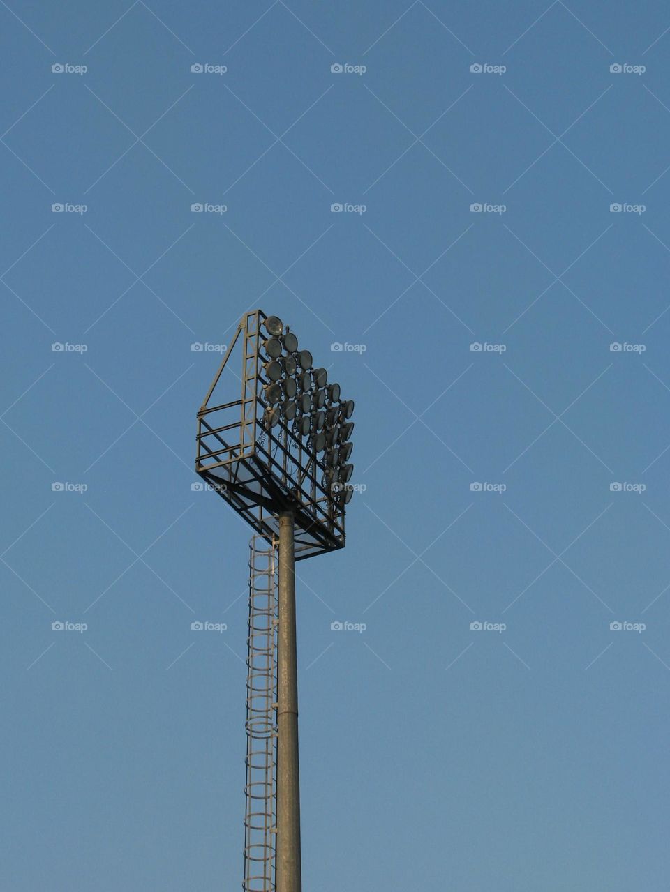 Tall stadium floodlights with a bright blue sky in the background