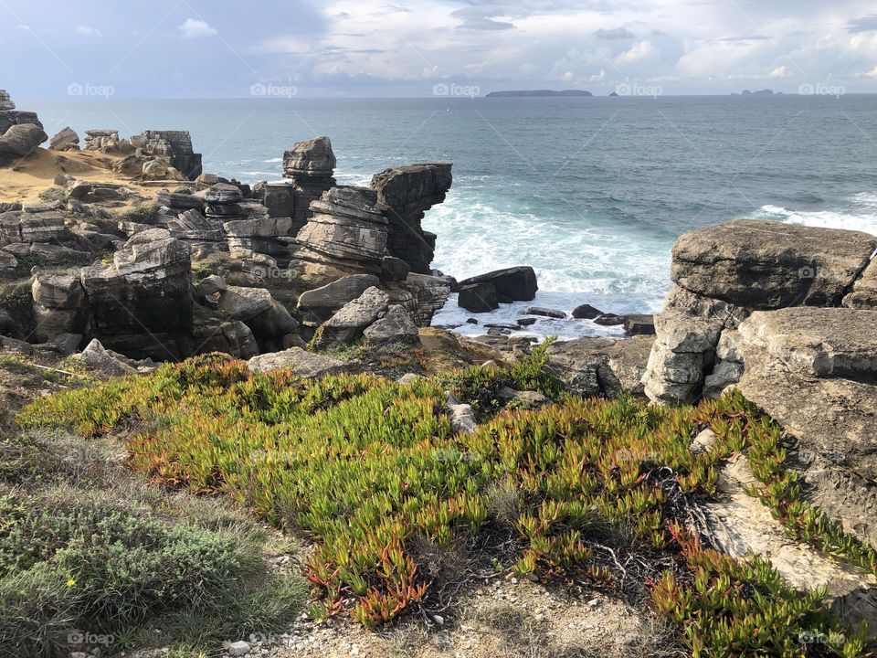 Green plants cover the rocks that jut out into the Atlantic Ocean at Peniche, with a view out to the Berlengas islands in the distance- no edits, no filter, #truephotos, true nature