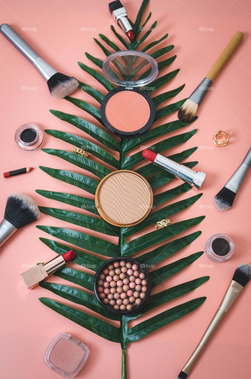 Beautiful view of a variety of natural cosmetics lying on a palm branch on a pink background, flat lay close-up.