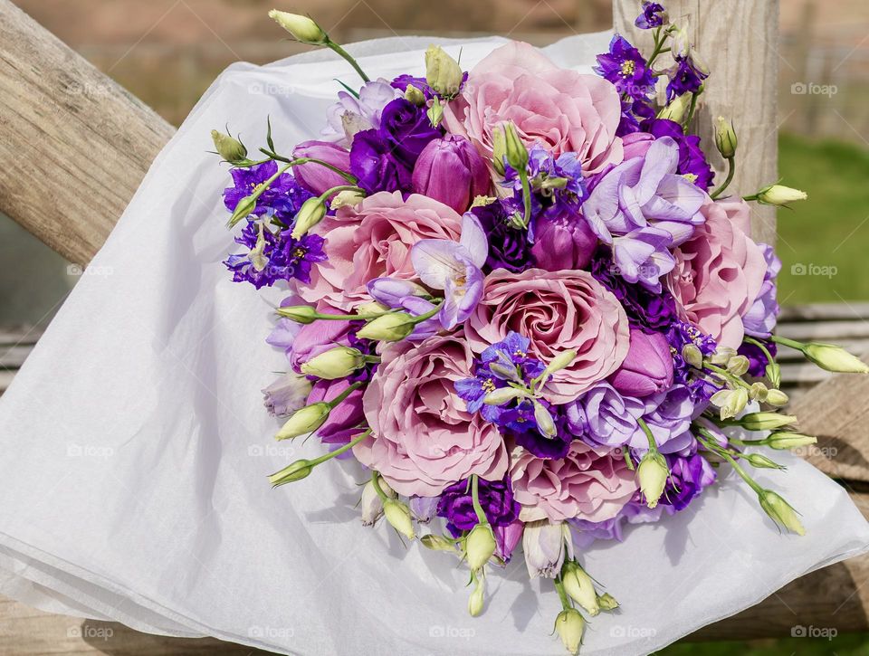 A wedding bouquet of pink & purple flowers, wrapped in white tissue paper