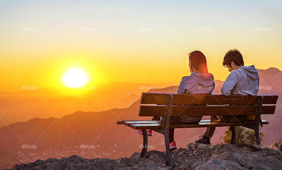 Couple watching sunset sitting in a bench at mountain top