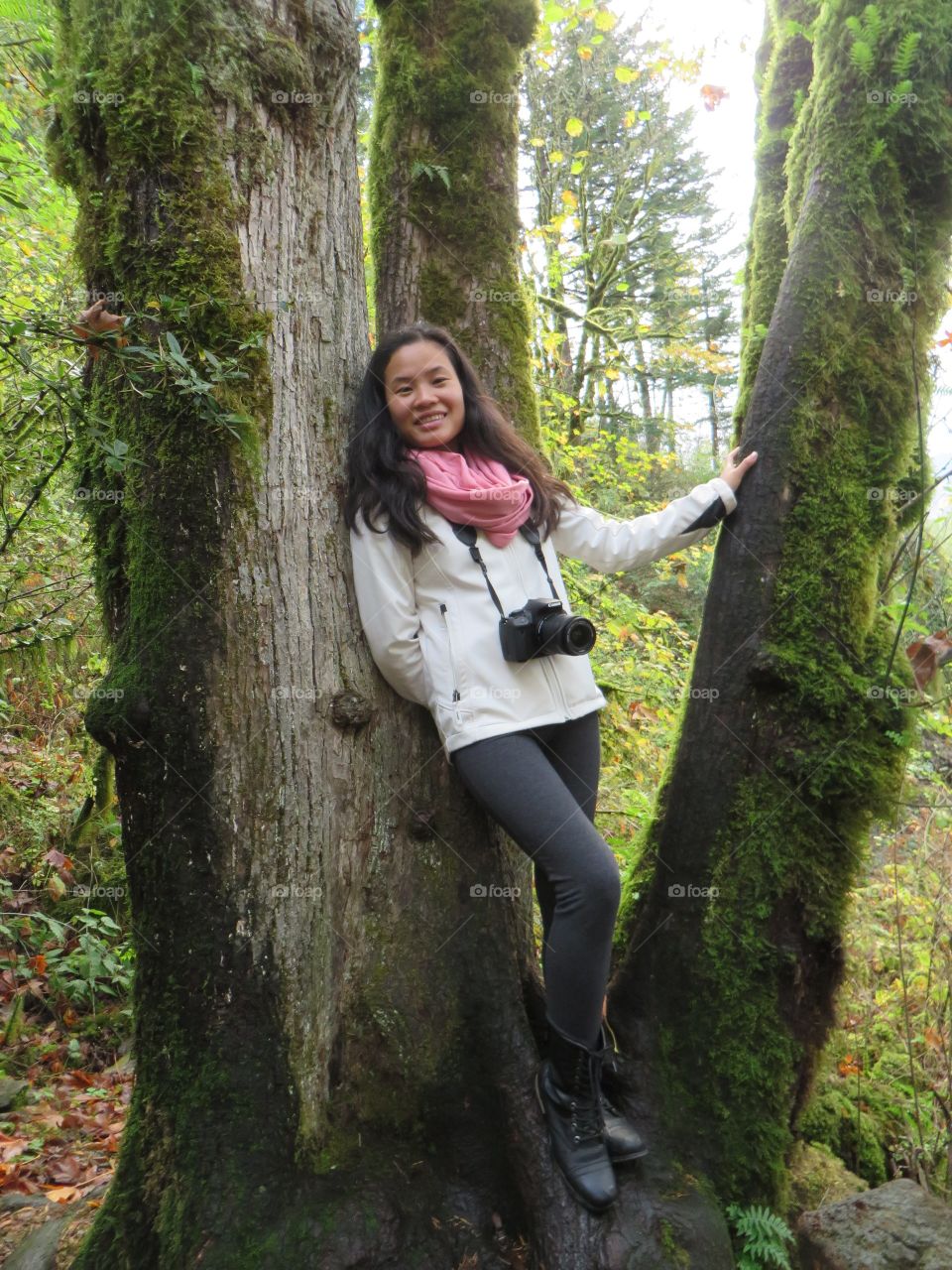 Asian woman standing near tree trunk with camera