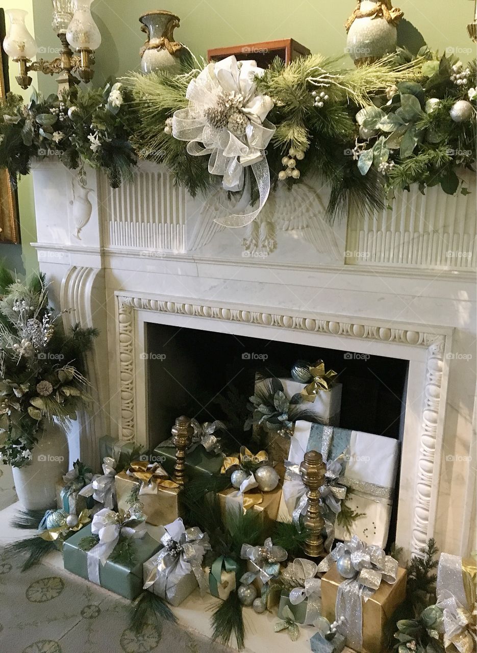 Perfectly wrapped presents complete with silver ribbons sit inside a marble fireplace with garland on the mantle