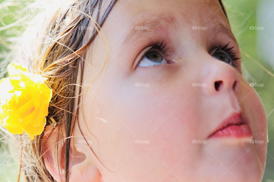 Darling close up photo of young girl with bright yellow flower in hair looking up. 