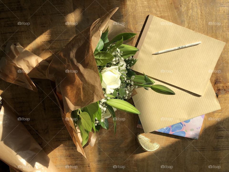 Wooden desk flat lay with rustic cream floral bouquet and notebooks with bright afternoon sunlight