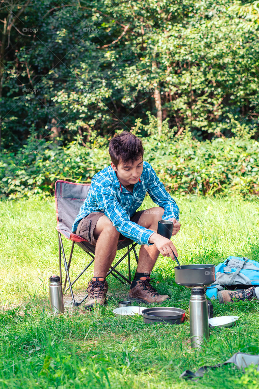 Spending a vacation on camping. Young man preparing a meal outdoor next to tent