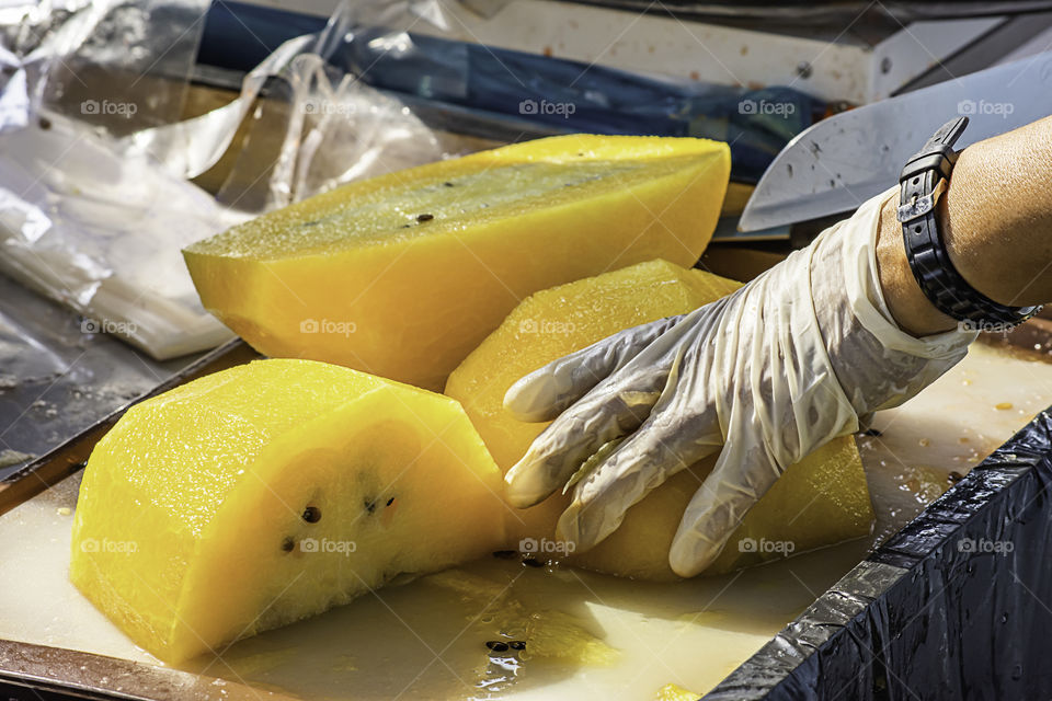 Hand holding yellow watermelon And use a knife to cut a piece.