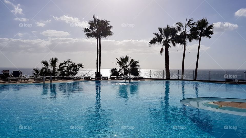 Beautiful swimming pool area with palm trees and view of the ocean in fair weather - fint poolområde med palmer och utsikt över havet i fint väder, perfekt för avkoppling 