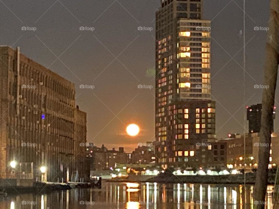 Light reflects on the still dark waters of Newtown Creek at night. The slick smooth as glass wetness is mirroring back the illumination from above. The full moon is glowing orange red, sometimes called a „devil moon“. 2021. Hypnotic Productions