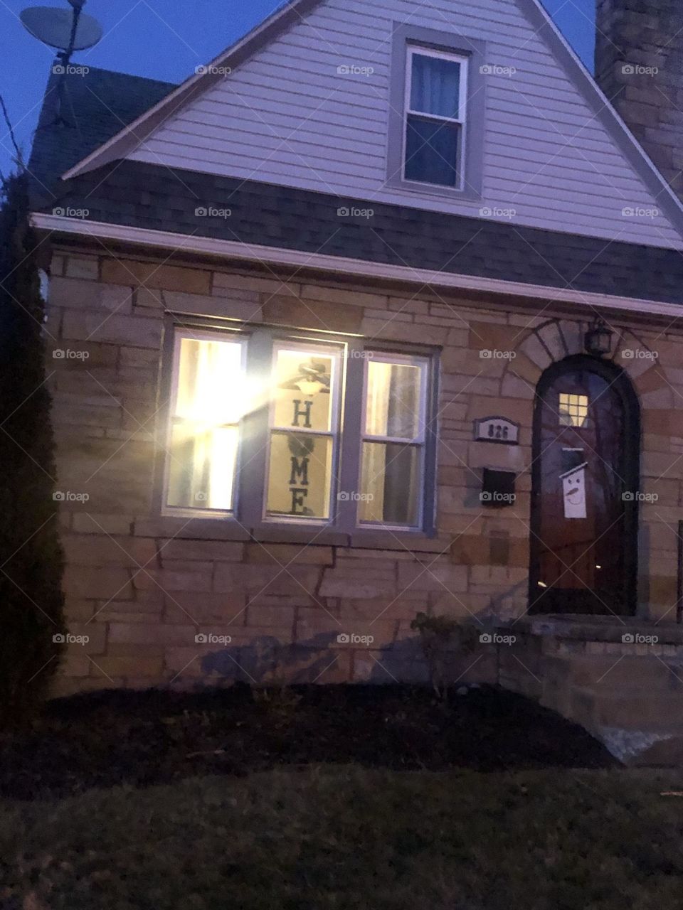 House with the wall hanging of the word home inside brick and white siding 