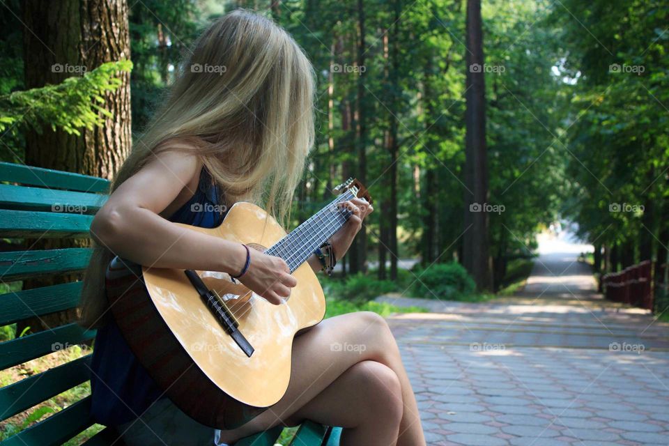 Girl learning to play guitar in a public park