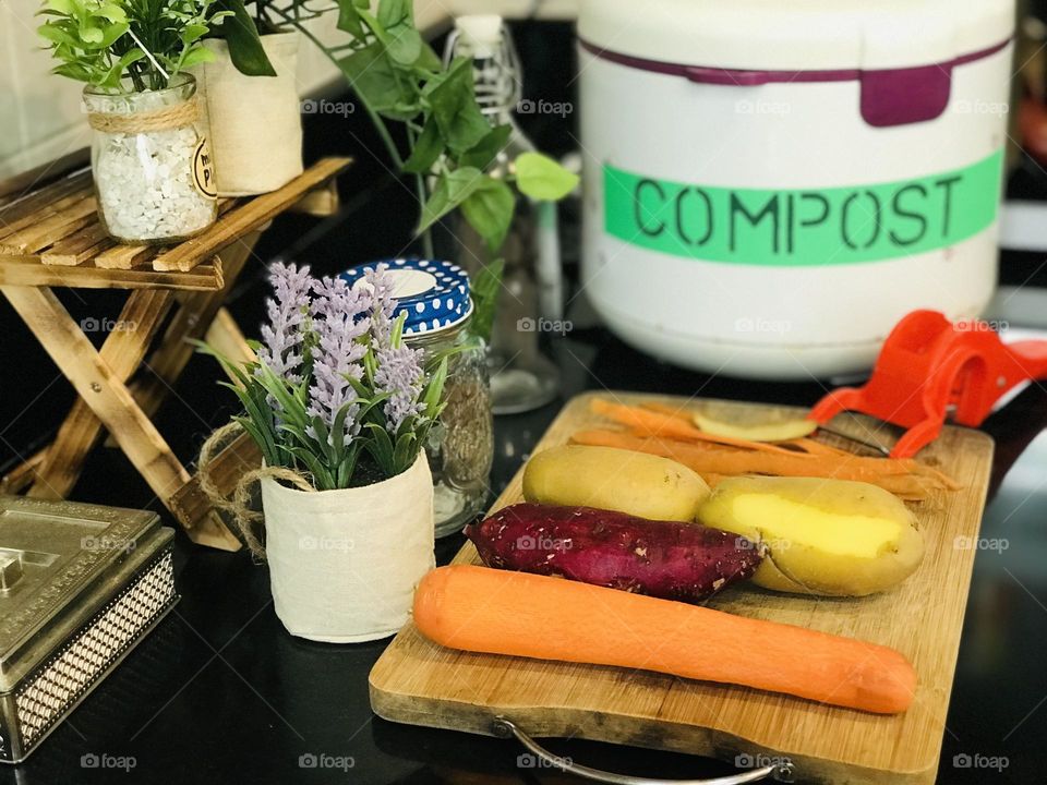 Making compost by daily kitchen trash is one of the way to reduce dump and it helps and save the environment . Here some root vegetables pealed out and some eco friendly flower pots and wooden stand and reusable containers around it.homemade compost 