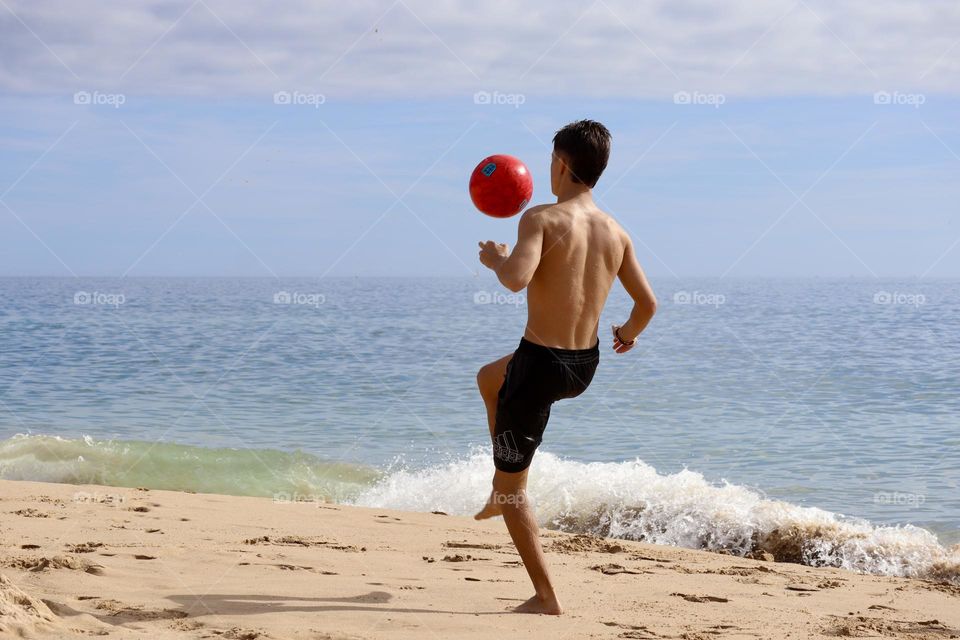 Kid bouncing a ball on the beach 
