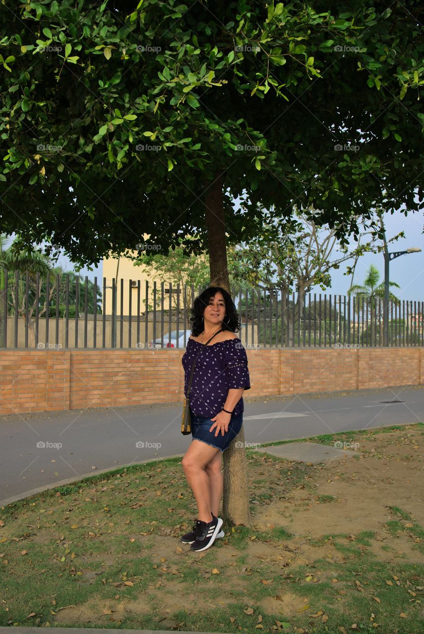 Woman model posing under the shade of a green tree in the daytime