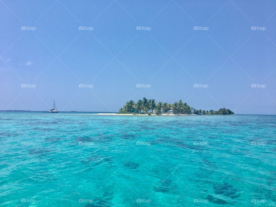 Remote island in Belize in Belize barrier reef.  A sailboat anchors by the beach.