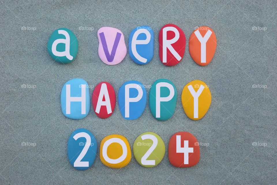 A very happy 2024 composed with multi colored stone letters and numbers over green sand