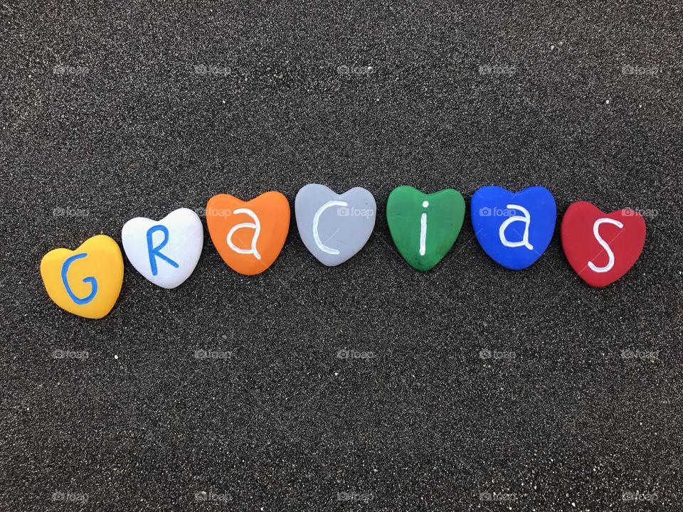 Gracias word with colored heart stones over black volcanic sand
