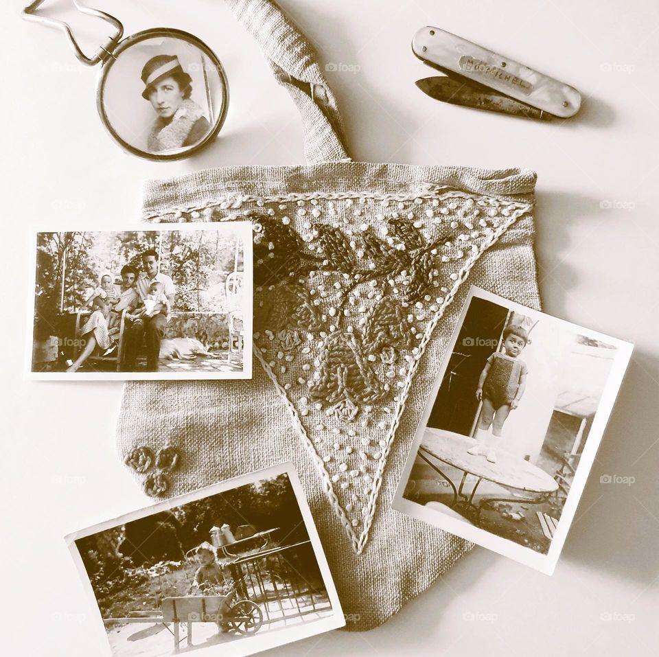 Sepia shot of a vintage flatlay placed on a cream surface composed of an handmade handbag, a mother-of-pearl penknife, a pocket magnifying glass and four old photos