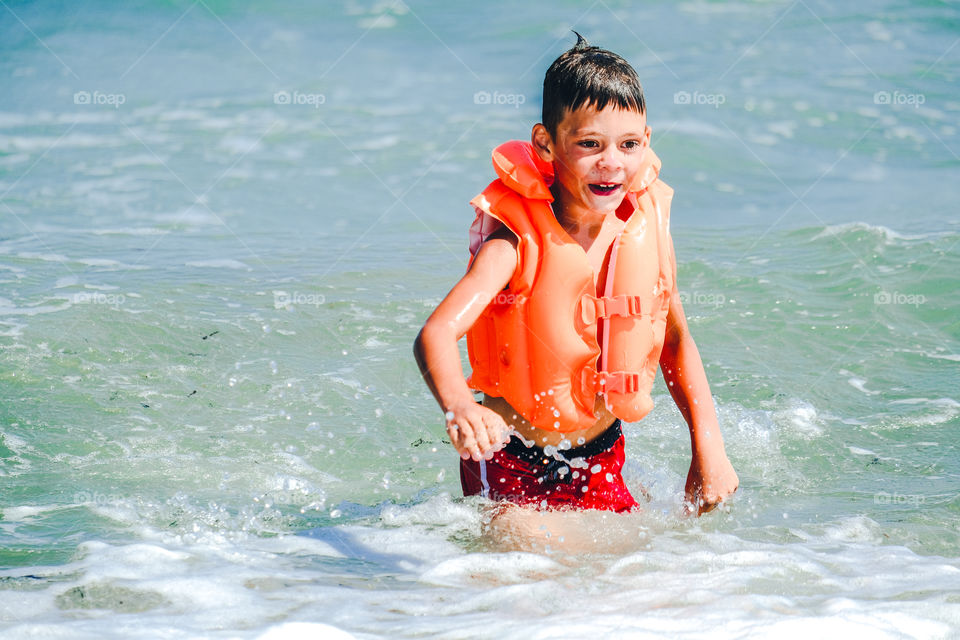 Smiling boy in orange inflatable vest swimming in the sea
