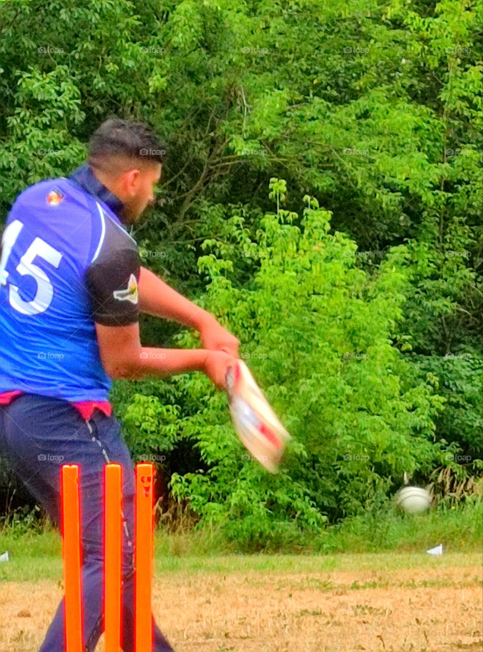 cricket training.  A player in a blue uniform hits a white ball