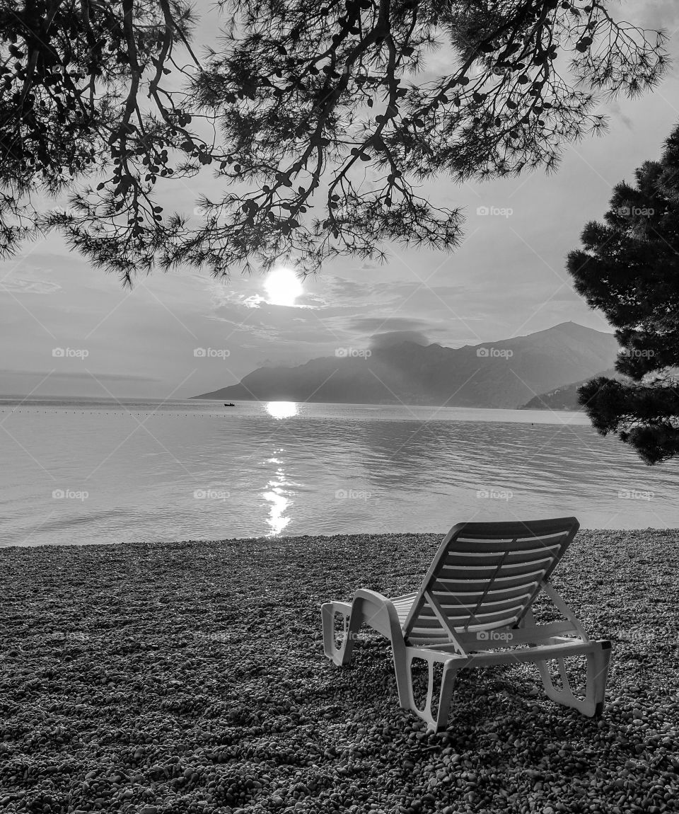 Monochrome landscape. Beach chair on a pebble beach against the background of a calm clean sea, mountains and sunset.  Summer vacation at sea.  Relax