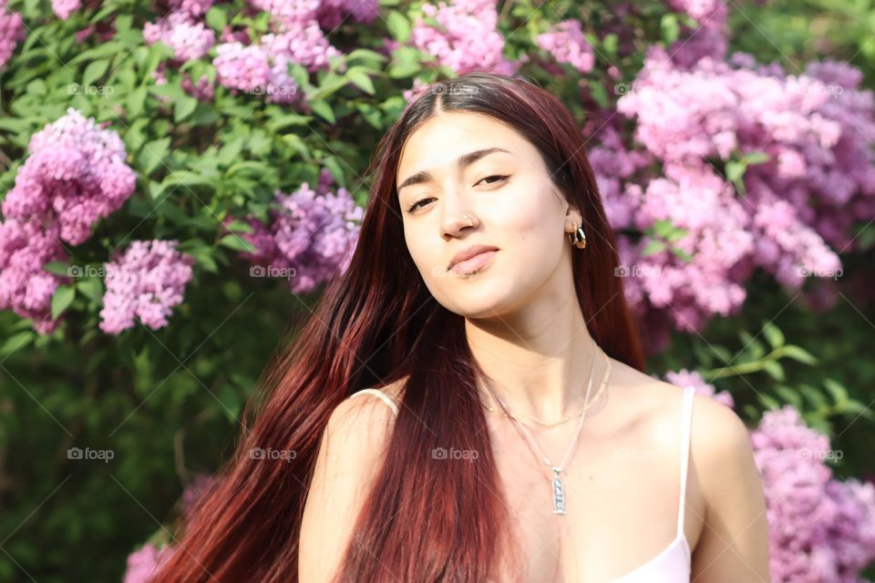 Young beautiful natural woman with long hair and blooming lilac on the background
