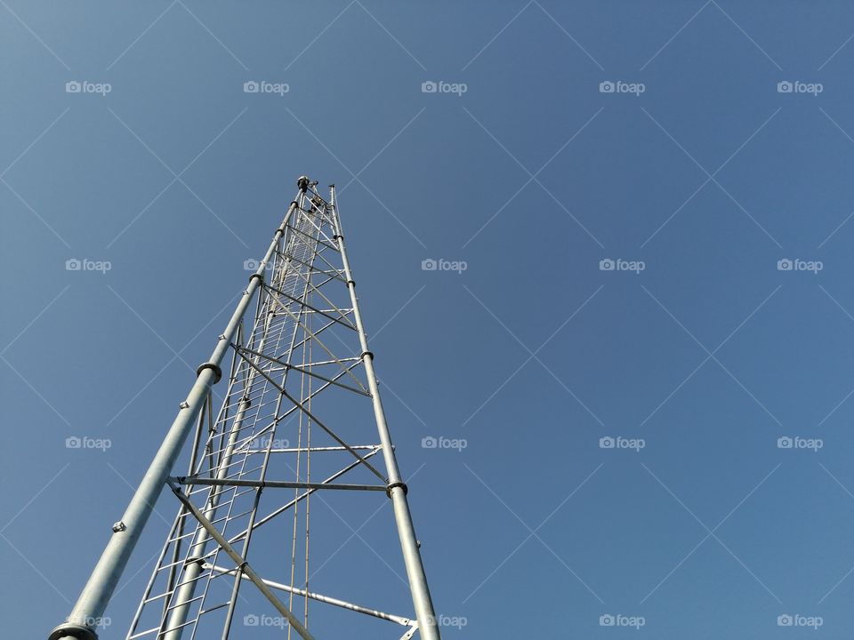 High Tower or pole of telecommunication working with high risk.Telecom radio tower over blue sky.