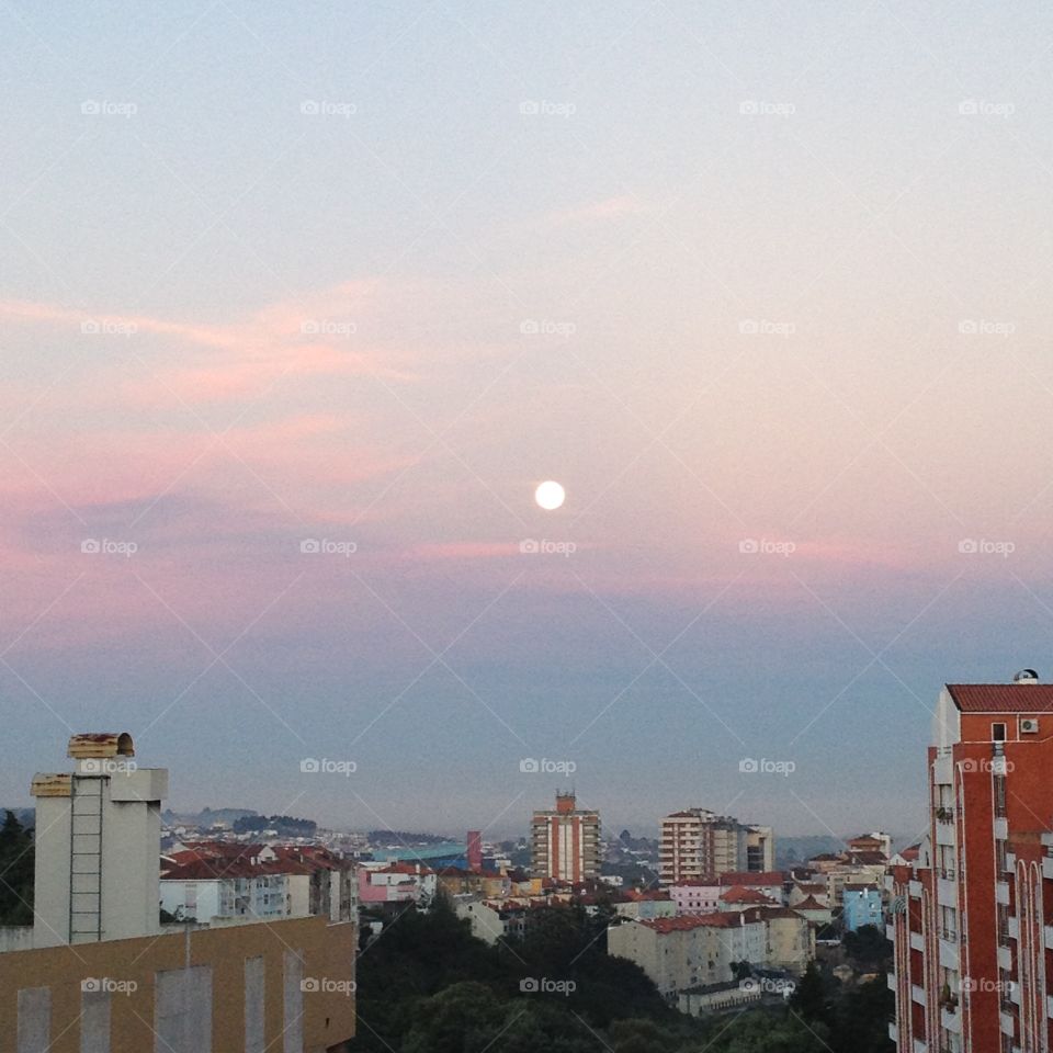 A clear visible moon at a colourful sunrise in the city