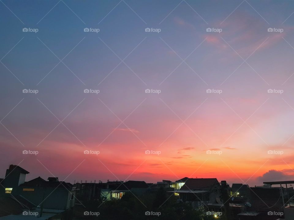 The view in morning, before sun rises, sky and clouds lokk red to yellow, quite bright, some of sky is blue-gray, house light are still on, atmosphere is quite cold, natural scenery, morning view