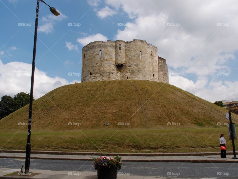 Clifford’s Tower, a local stone landmark in York in England, sits majestically on top of a hill on a sunny day. 