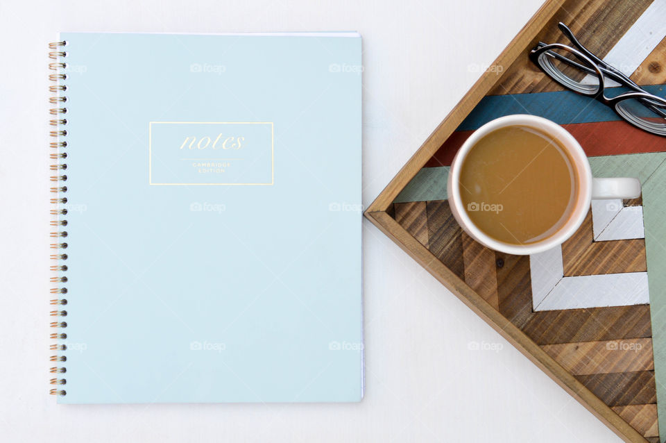 Flat lay of a notebook next to a cup of coffee and glasses on a wooden tray