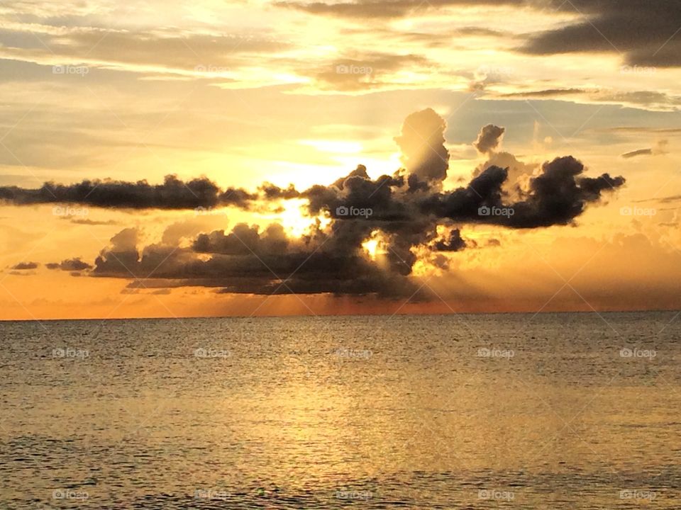Clouds are silhouetted against a warm sunset on the Gulf of Mexico horizon, as contrasting beams are pulled down to the sea. 