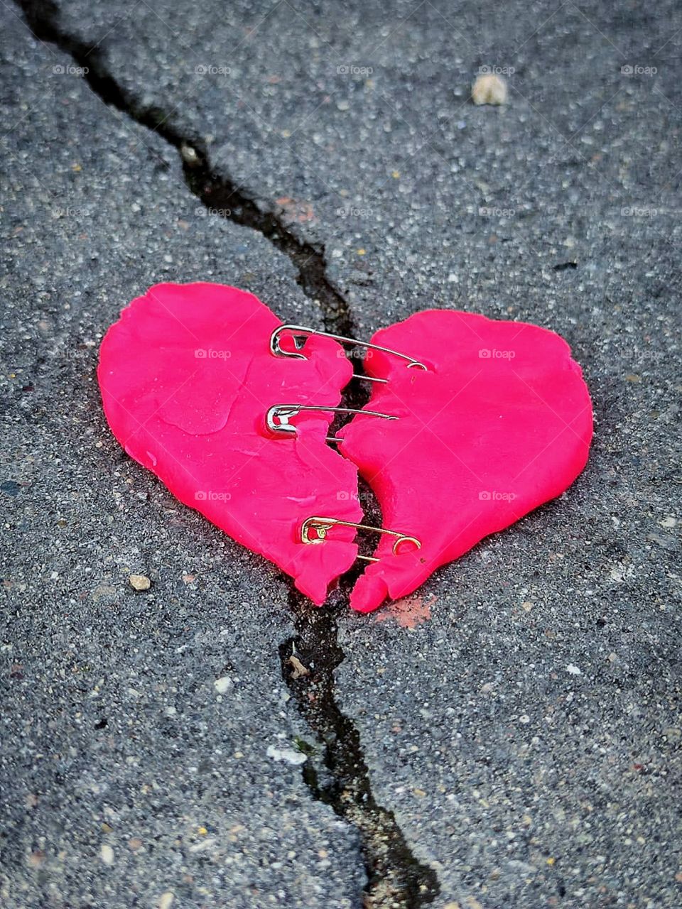 Crack in the asphalt. On the cracks lies a red "torn" heart, which is fastened with pins