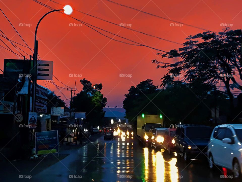 Nighttime view of highway, heavy rain, road surface reflecting light, street lighting shimmering, car lighting, road mirroring light, heavy traffic, vehicle queues, visible vehicle headlamps luminous, colorful light from vehicles, shiny car lighting,