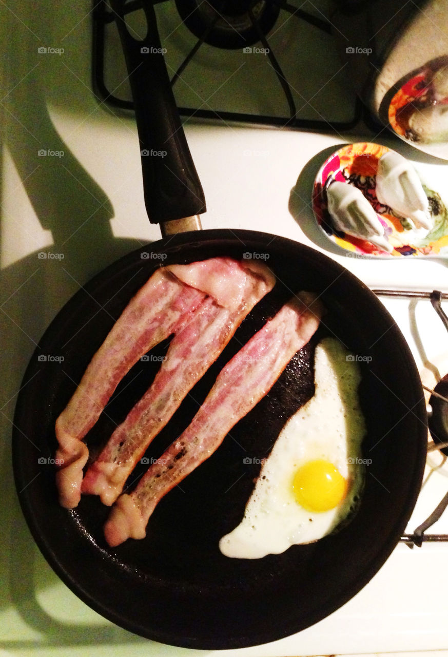 American breakfast of bacon and eggs cooking in a frying pan