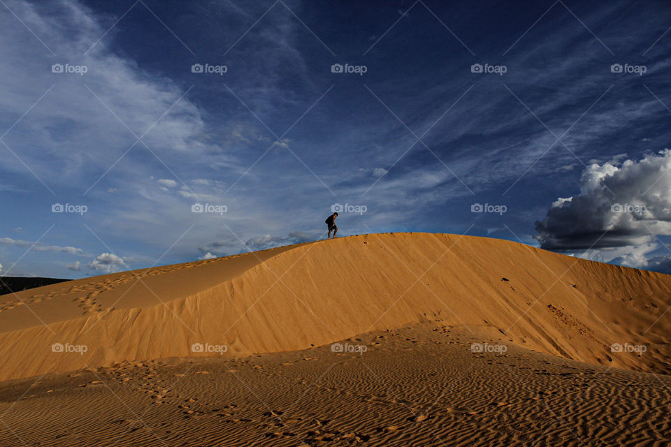 wide view of a man climbing a sand bank of Jalapão in Brazil, in contrast with a beautiful blue sky