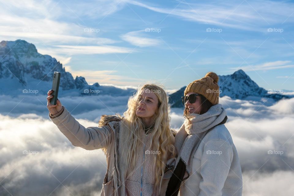Two young women taking a selfie high up in the mountains in winter
