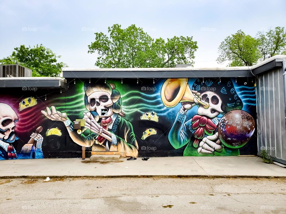 Multiple musician skeletons street art painting with multiple tree tops in the background.