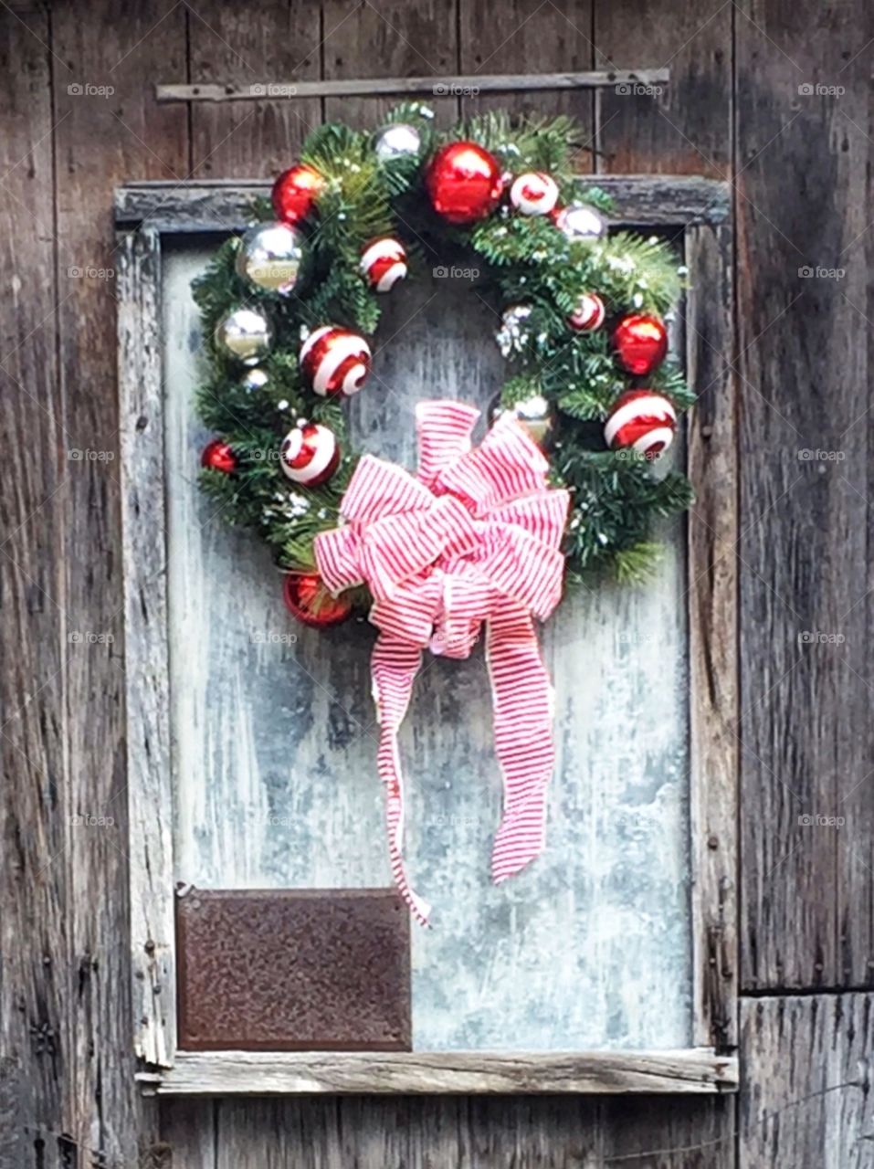 Christmas wreath decoration with red ornaments and bow hanging on an old weathered wooden door