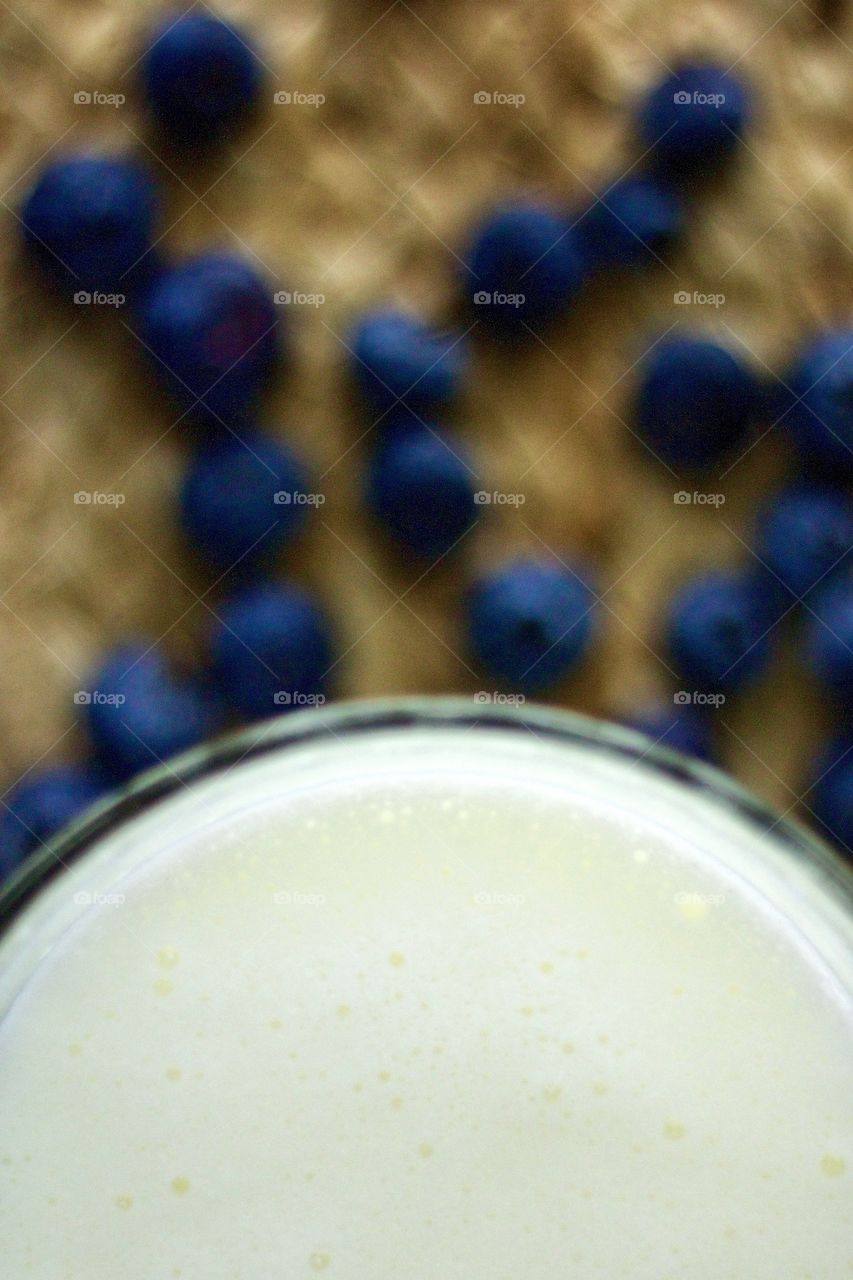 Overhead closeup of dairy kefir with blurred background of blueberries on a natural fiber woven surface