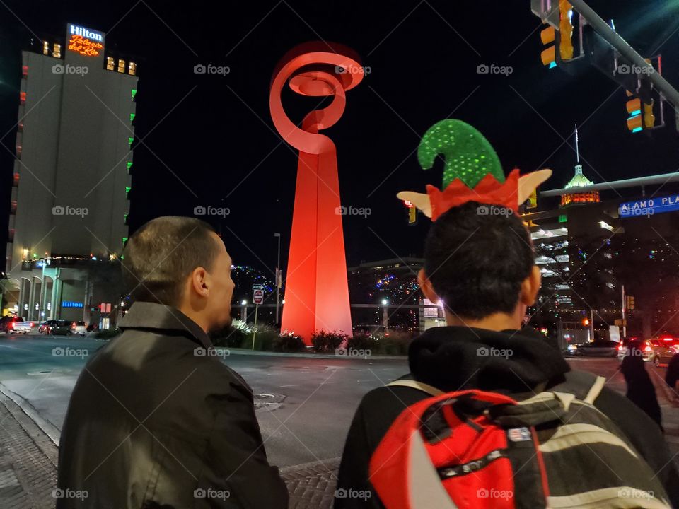 Brothers visiting downtown San Antonio, Texas for the holidays in front of the friendship sculpture that was a gift from Mexico.  One brother is wearing an elf hat.